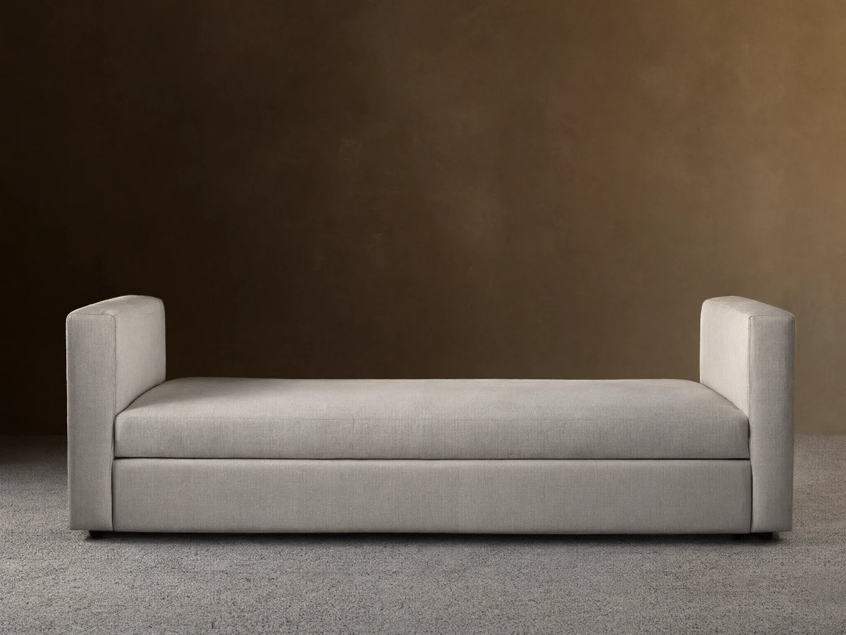 Light beige Remington Trundle Sleeper Daybed with two low, rounded armrests, on a wooden floor against a beige wall.
