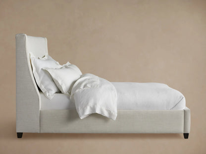 Side view of the light gray Atlyn Bed, upholstered, with a wingback headboard and white bedding.