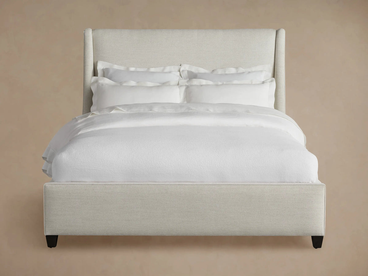 Light beige upholstered Atlyn Bed, featuring a tall, winged headboard and a low profile, dressed with white bedding.