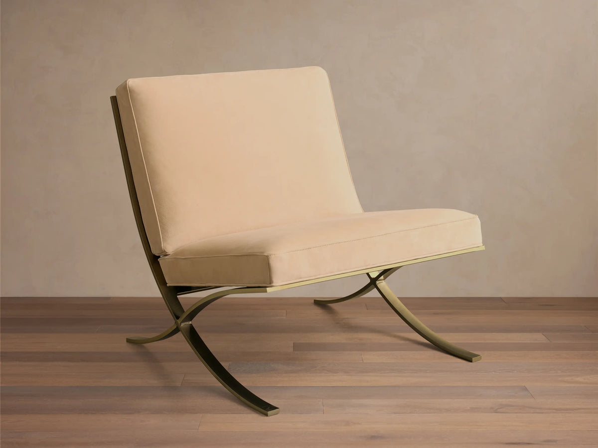 Front view of a light beige Moxie Leather Chair with tufted leather cushions and a curved, brass-finished stainless steel frame.