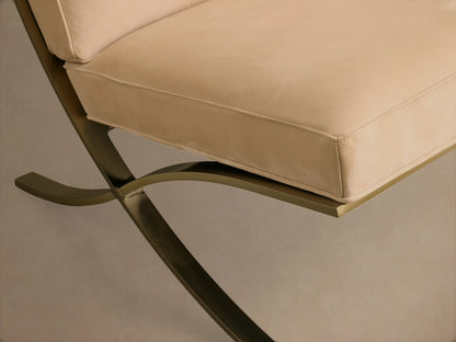 Close-up of the light beige leather seat cushion with piped edges and the bronze metallic X-shaped base of the Moxie Leather Chair.