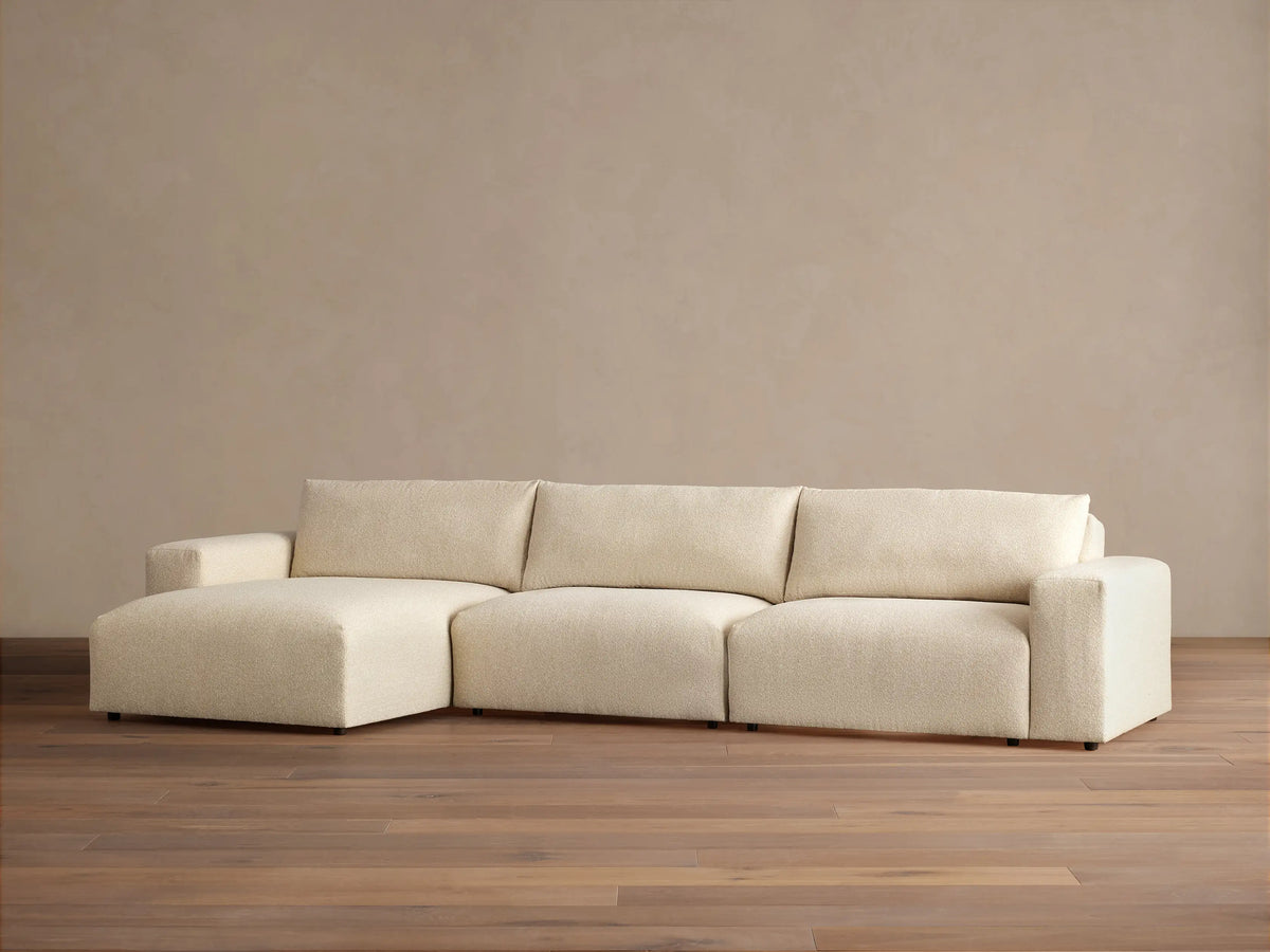 Keegan Tailored Three-Piece Chaise Sectional in textured cream fabric. Left-facing chaise, two seats, light brown wall, wood floor.