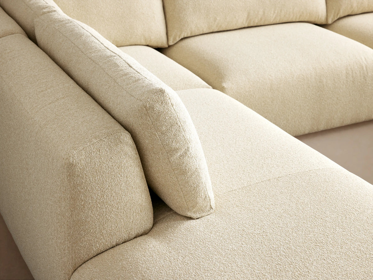 Keegan cream L-shaped 4-piece bumper sectional sofa on a wooden floor against a warm beige wall.