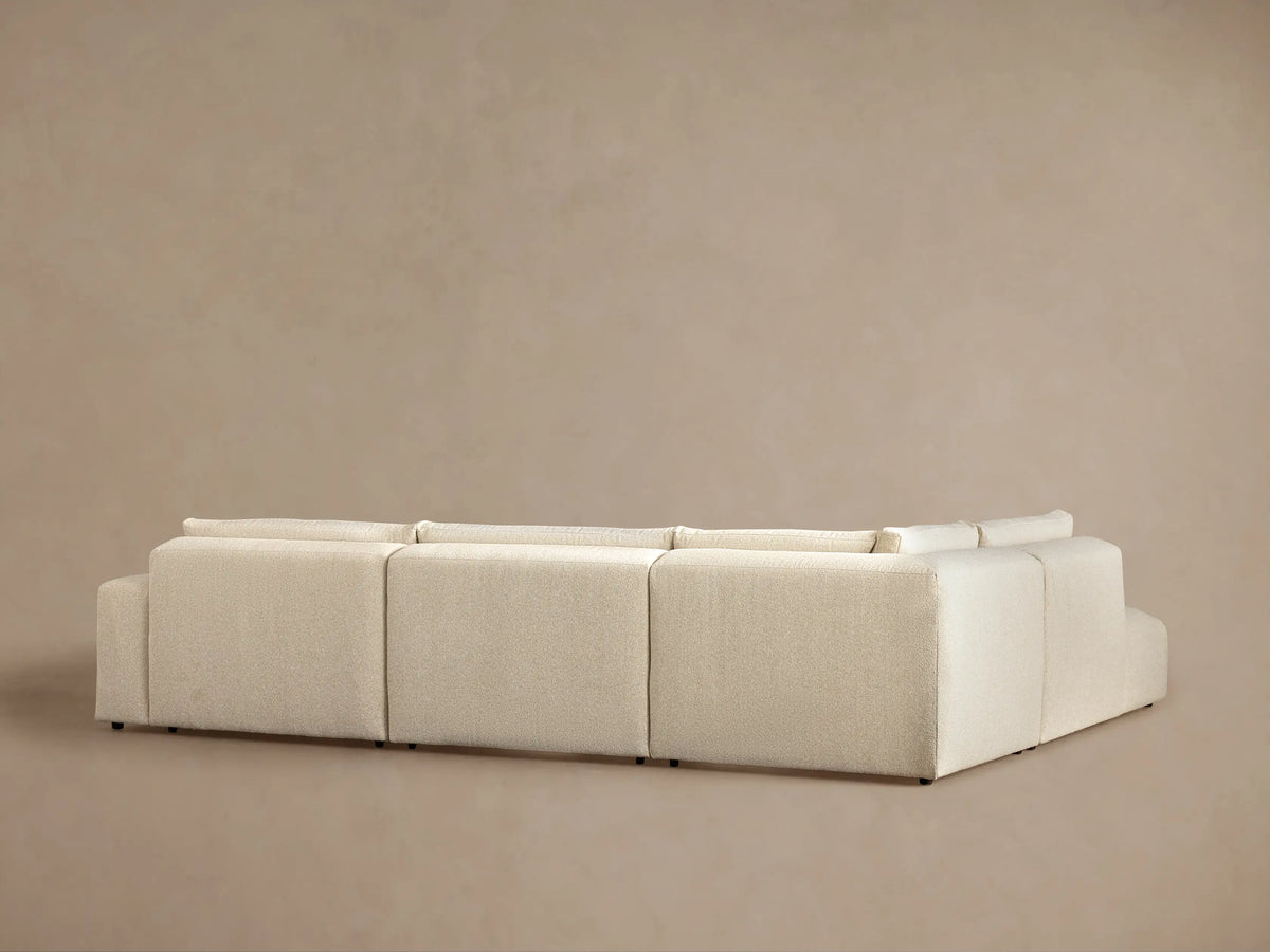 Angled view of a cream-colored Keegan Tailored Four-Piece Bumper Sectional, highlighting its textured fabric, plush backrest, and seat cushion.