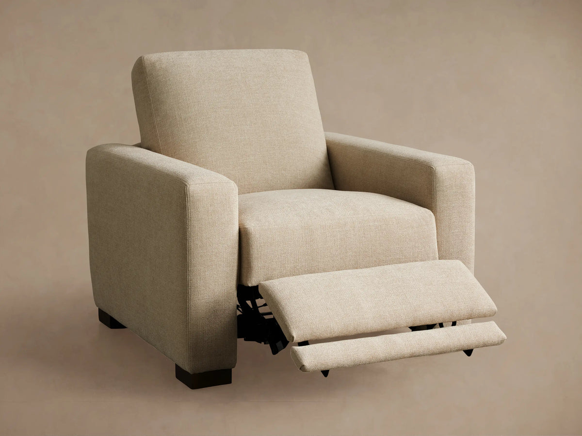 Rear three-quarter view of the beige Remington Motion Recliner with dark wooden feet and a side control panel.