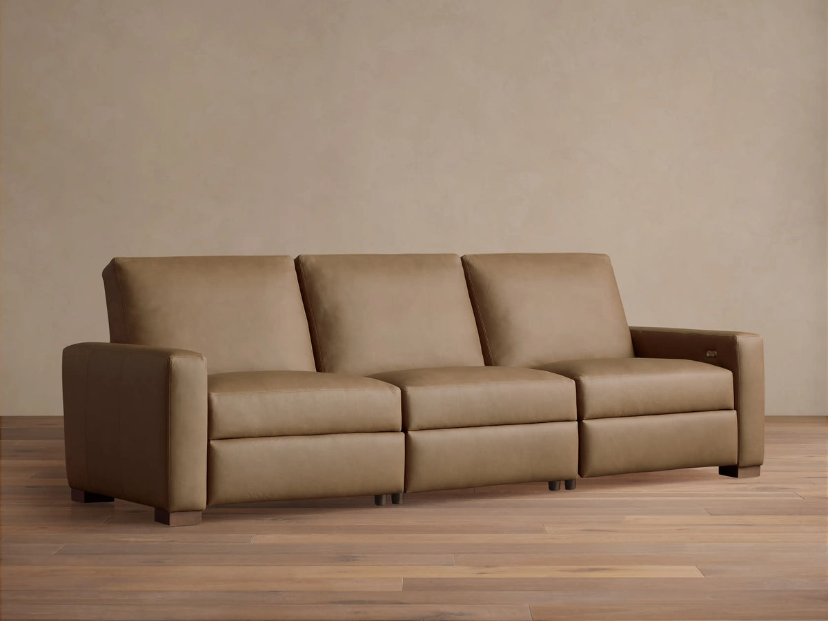 Remington Three-Piece Motion Sofa in tan leather, featuring clean lines and square arms, sits centered on a wood floor.