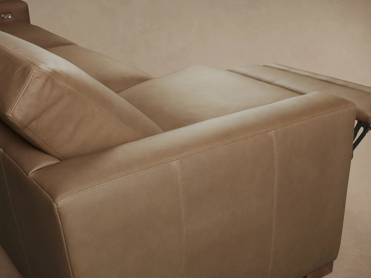 Close-up of Remington Leather Motion Sofa's light brown leather backrest, silver recliner button, and seat cushion.