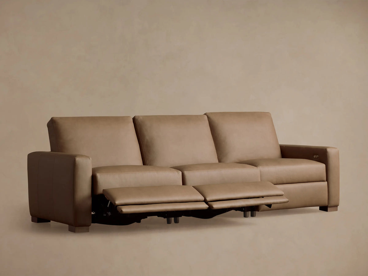 Back view of a light tan leather Remington Three-Piece Motion Sofa with three connected reclining sections against a plain wall.