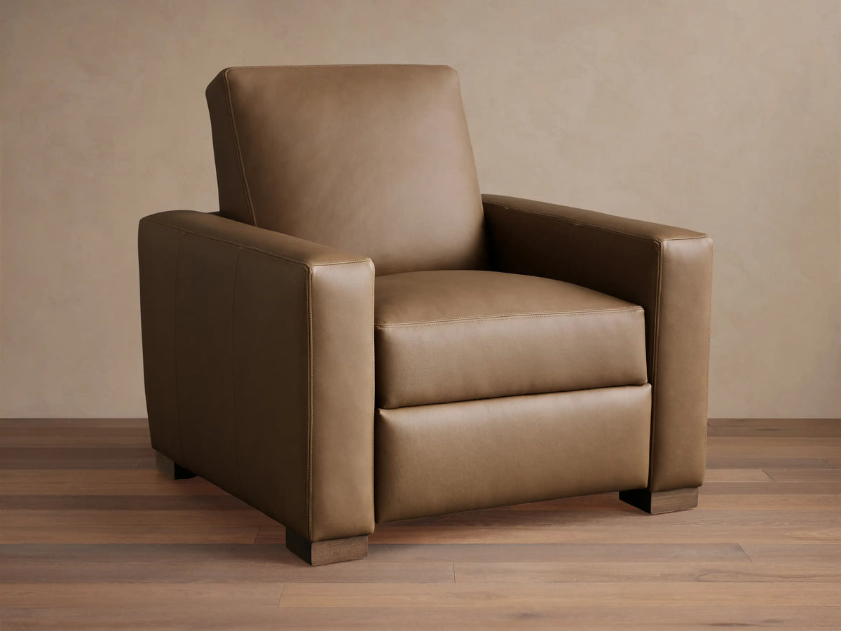 Light brown leather Remington Motion Recliner, a modern armchair with wide arms, seen from the front on wood floor.