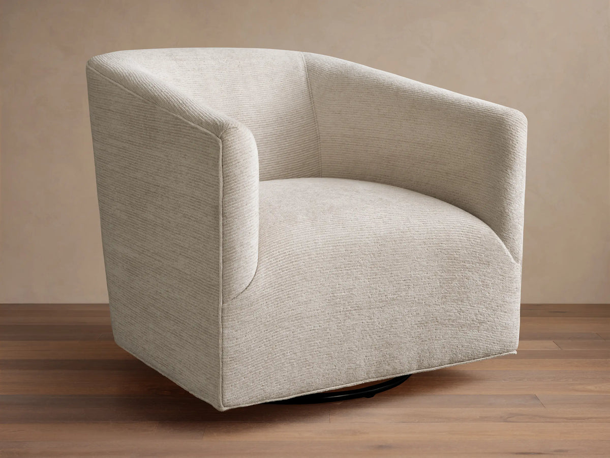 Ellison Swivel Glider, light beige textured fabric with curved arms and back, on a black swivel base on wood.