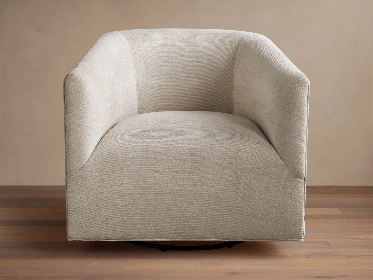 Ellison Swivel Glider, light beige textured fabric with curved arms and back, on a black swivel base on wood.