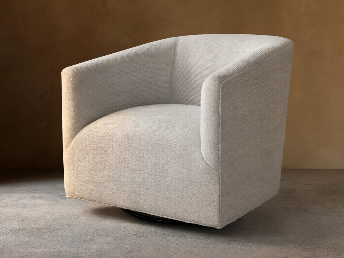 Ellison Swivel Glider, light beige textured fabric with curved arms and back, on a black swivel base on wood.