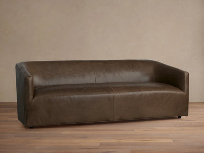 Brown Ellison Leather Sofa with a sleek, modern design. Features smooth, continuous curves and a slight sheen, set on a wooden floor.