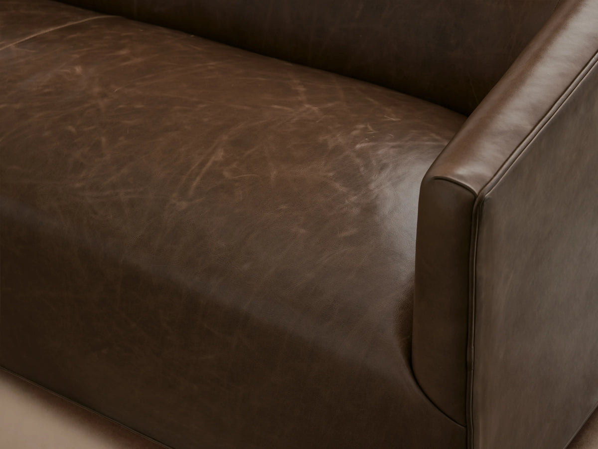 Ellison Leather Sofa in rich brown leather, featuring a sleek, low-profile design with gently sloped arms, set on a wooden floor.