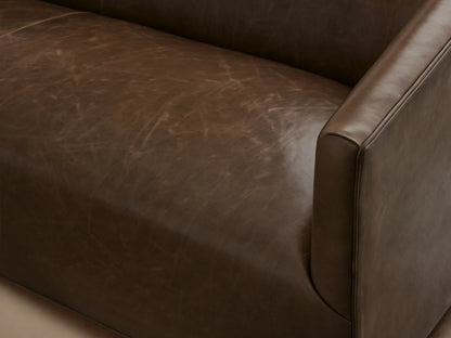 Ellison Leather Sofa in rich brown leather, featuring a sleek, low-profile design with gently sloped arms, set on a wooden floor.