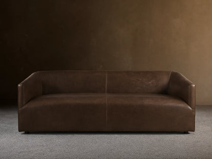 Brown Ellison Leather Sofa with a sleek, modern design. Features smooth, continuous curves and a slight sheen, set on a wooden floor.