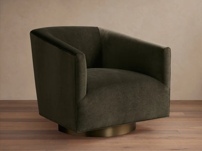 Dark brown Ellison Metal Plinth Swivel Chair with a rounded, cushioned backrest and armrests, on a brass-toned swivel base, against a wooden floor.