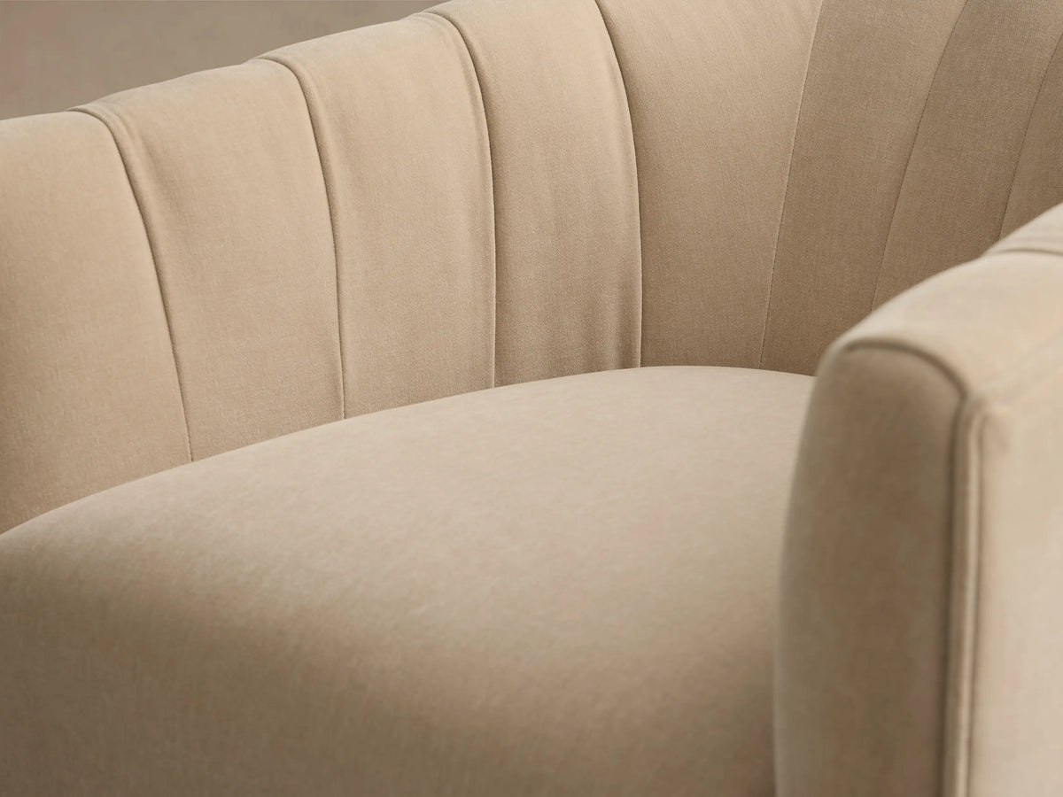 Close-up of the beige Ellison Channel-Stitched Metal Plinth Swivel Chair™ with its channel-stitched back and curved armrest.