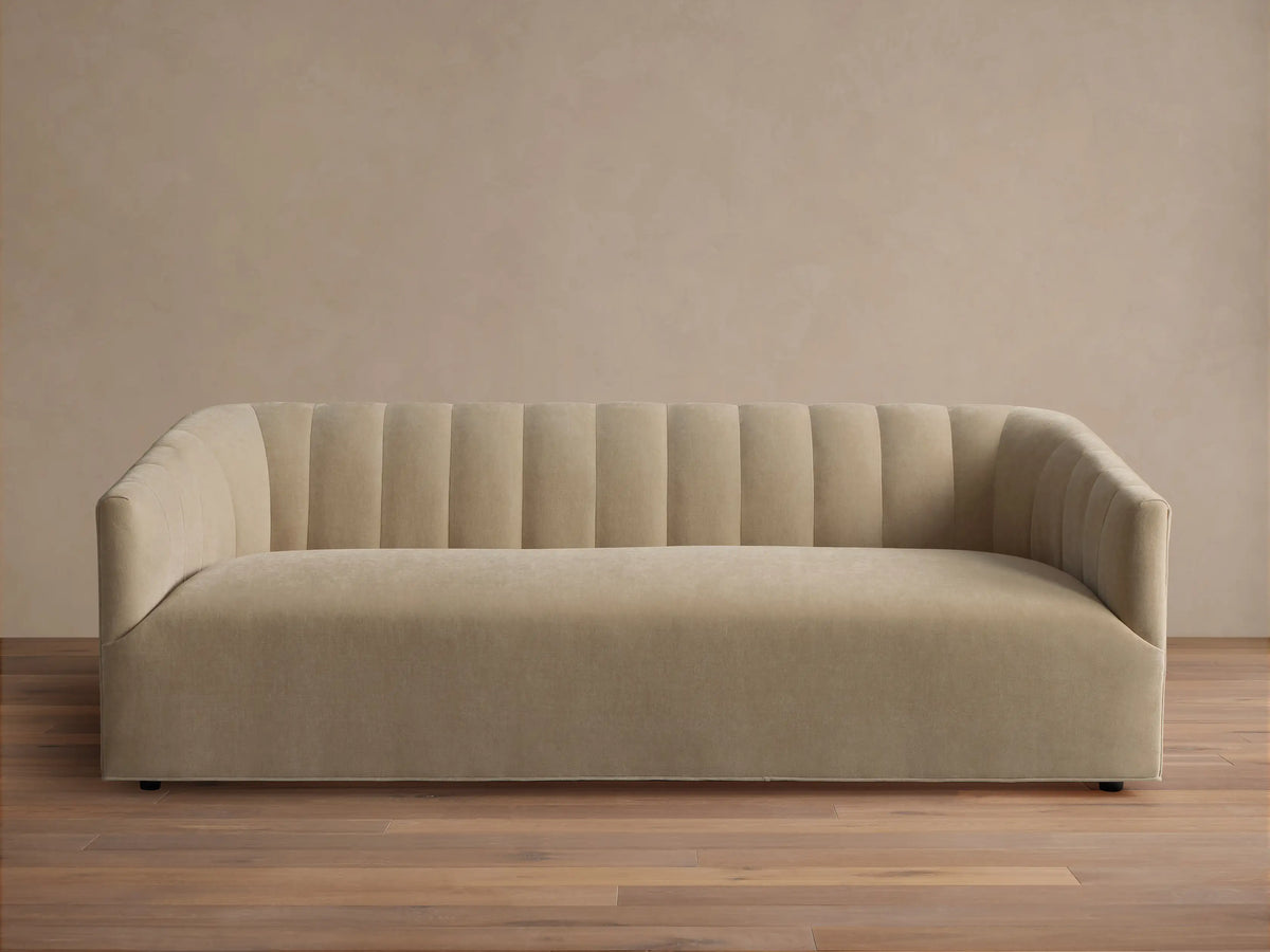 Pale tan Ellison Channel-Stitched Sofa, front view, with vertical channels on backrest & inner arms, on wood floor against light wall.