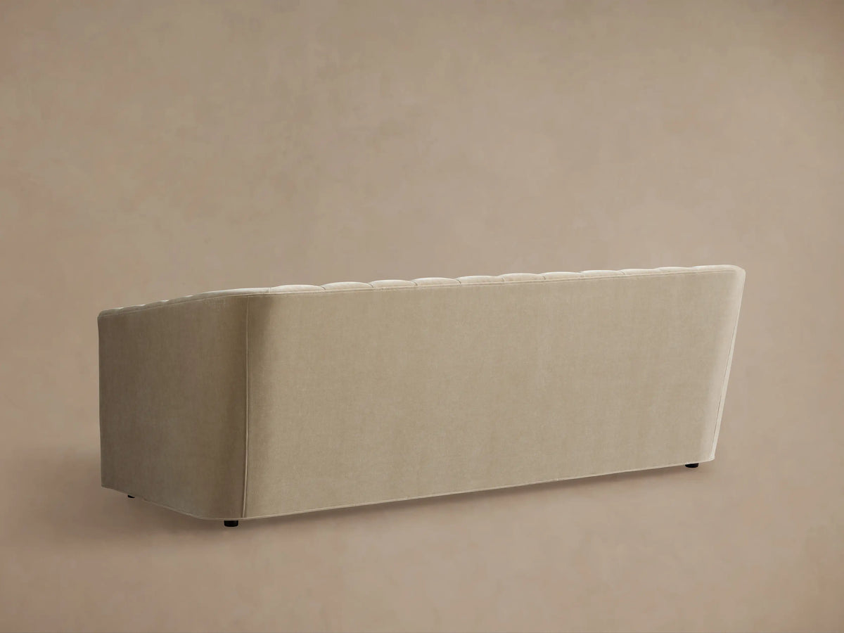 Ellison Channel-Stitched Sofa. Curved, light beige fabric backrest with vertical channels, rounded arm, against a beige wall.