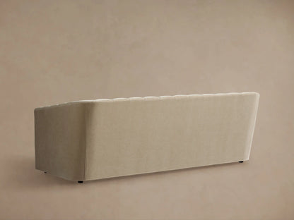 Ellison Channel-Stitched Sofa. Curved, light beige fabric backrest with vertical channels, rounded arm, against a beige wall.