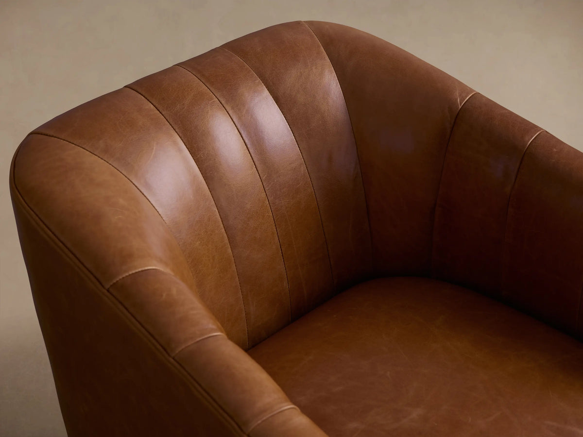 Ellison Swivel Glider, rich tan leather with vertical channel stitching on curved back and arms, on a black swivel base.