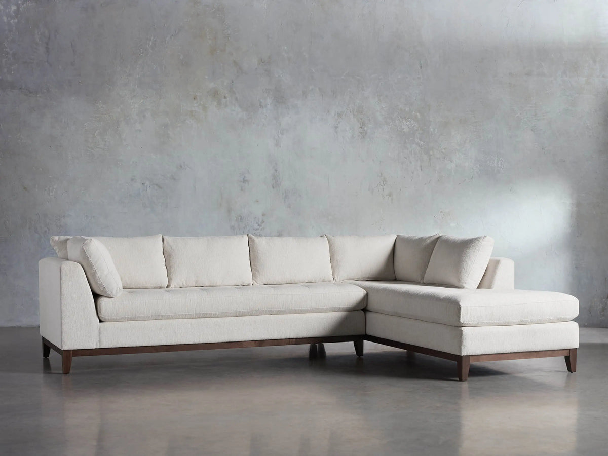 Cream Bryden Two-Piece Daybed Sectional with textured fabric, L-shaped, dark wood base, shown in front of a gray wall.