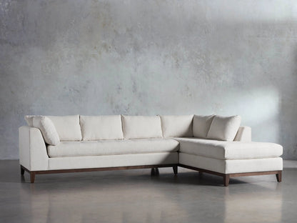 Cream Bryden Two-Piece Daybed Sectional with textured fabric, L-shaped, dark wood base, shown in front of a gray wall.