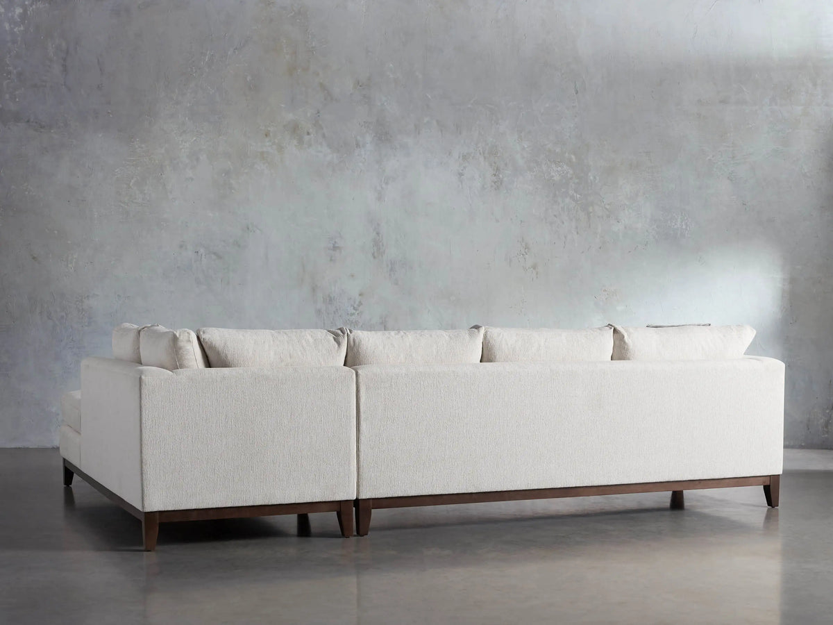 Bryden Two-Piece Daybed Sectional, light beige, L-shaped, with dark wood legs, on a concrete floor against a gray wall.