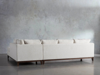 Bryden Two-Piece Daybed Sectional, light beige, L-shaped, with dark wood legs, on a concrete floor against a gray wall.