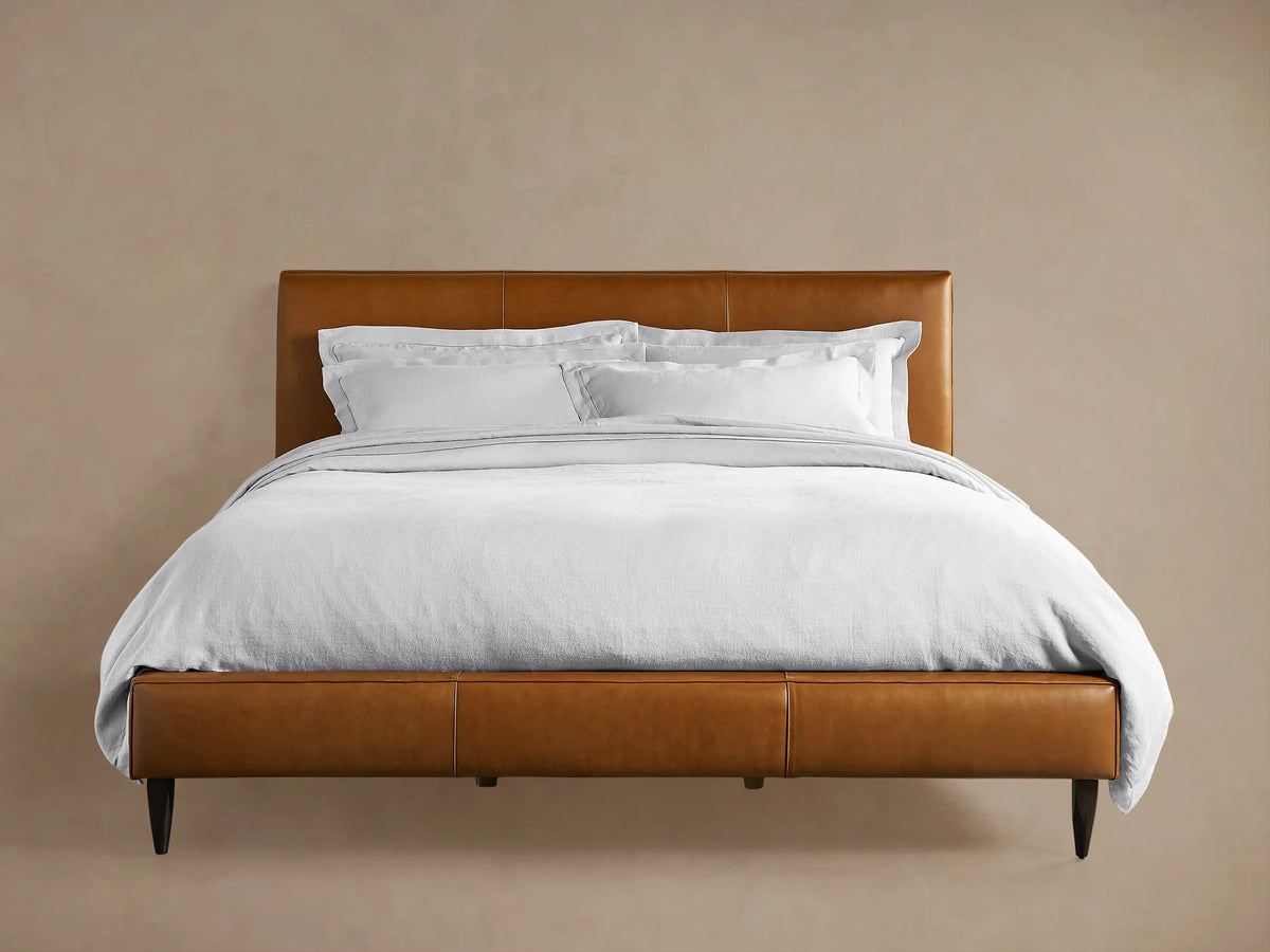 Andes Leather Bed: A stylish, modern bed frame in rich brown leather, with a padded headboard & white bedding, on wood floor.