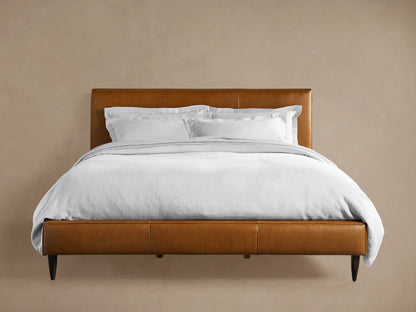 Andes Leather Bed: A stylish, modern bed frame in rich brown leather, with a padded headboard & white bedding, on wood floor.