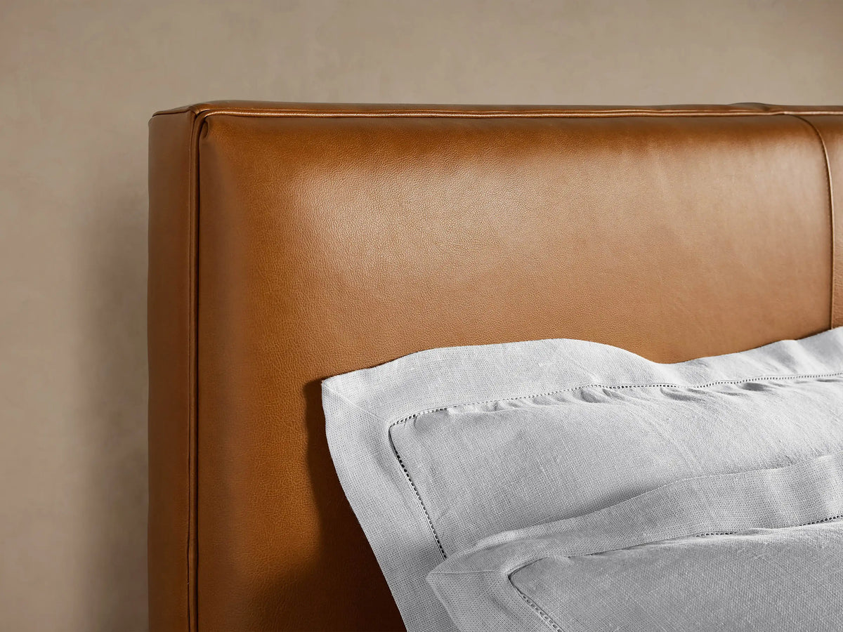 Andes Leather Bed, full view. Rich brown leather headboard and frame with stitched details, white pillows and duvet. Dark tapered legs.