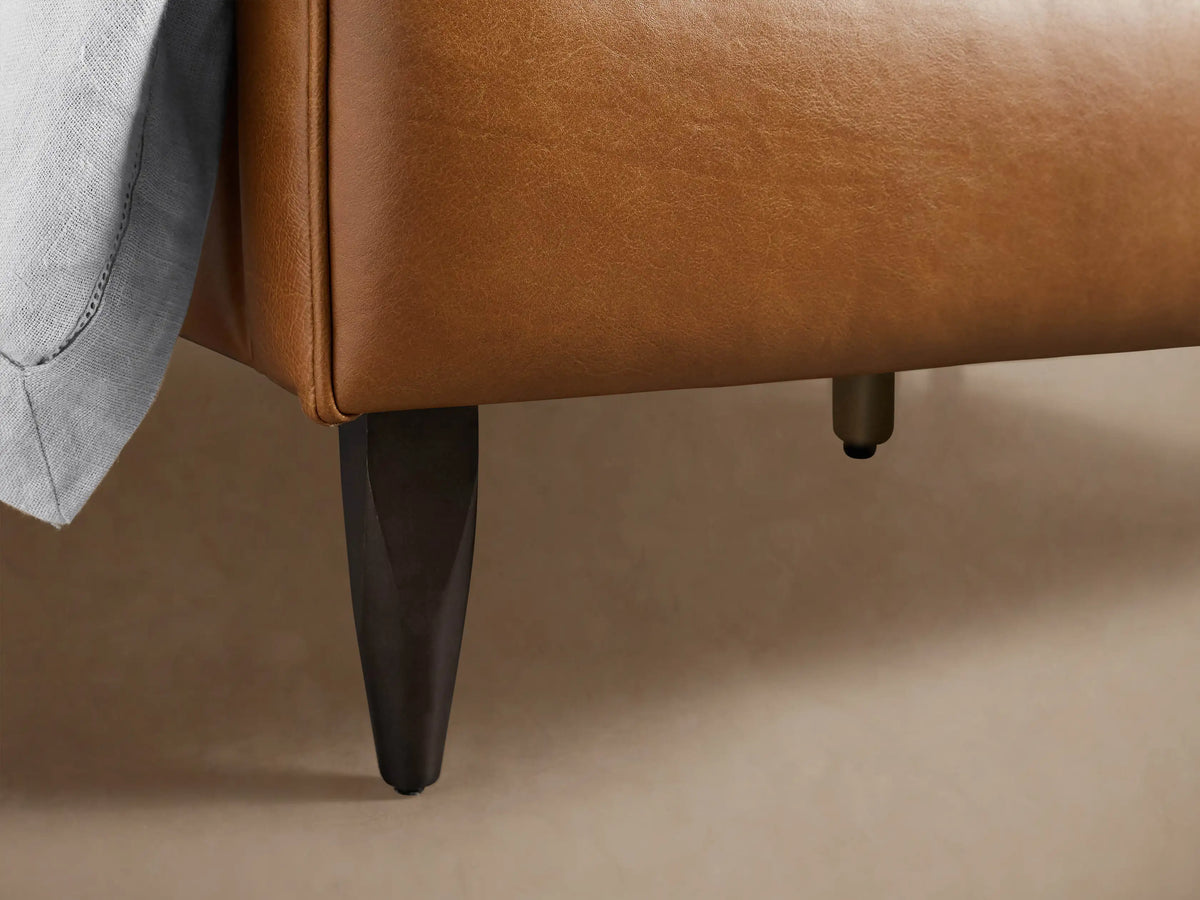 Close-up of the Andes Leather Bed's rich brown leather headboard with piped detail and a light gray pillow.
