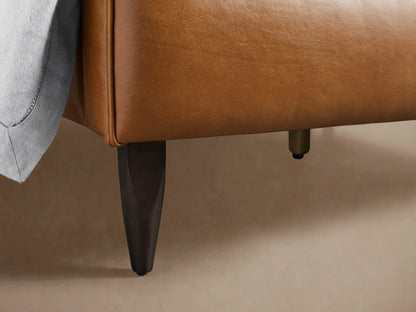 Close-up of the Andes Leather Bed's rich brown leather headboard with piped detail and a light gray pillow.