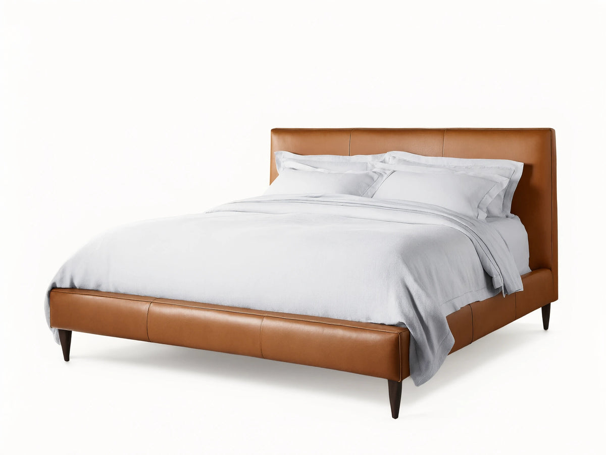 Andes Leather Bed: A stylish, modern bed frame in rich brown leather, with a padded headboard & white bedding, on wood floor.
