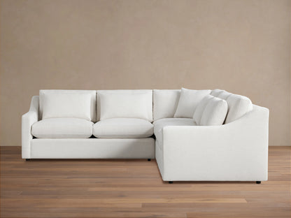Alt text: Ashby Three-Piece Corner Sectional in off-white fabric, featuring three seat cushions and backrests, displayed on a wooden floor against a beige wall.