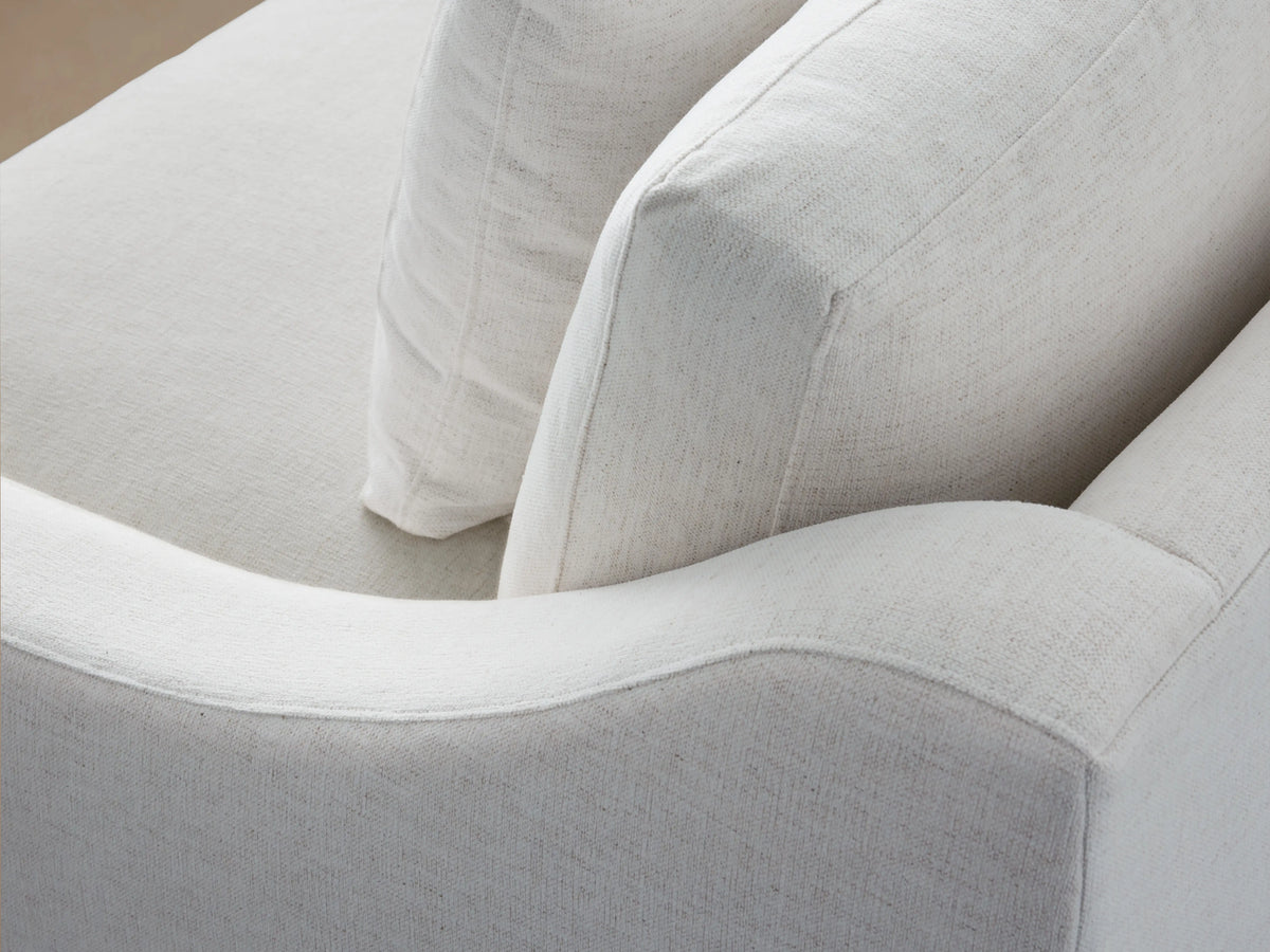 Alt text: Close-up of the Ashby Two-Piece Sectional in light fabric, showing a curved armrest and backrest with soft, textured upholstery.