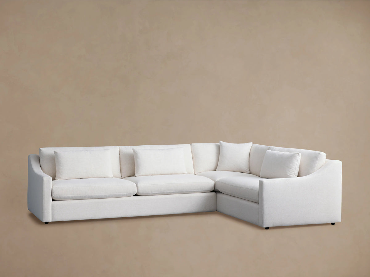 Alt text: Ashby Two-Piece Sectional in off-white fabric against a beige background, featuring three seat cushions and multiple backrest pillows with a right-angle design.