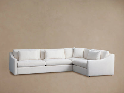 Alt text: Ashby Two-Piece Sectional in off-white fabric against a beige background, featuring three seat cushions and multiple backrest pillows with a right-angle design.