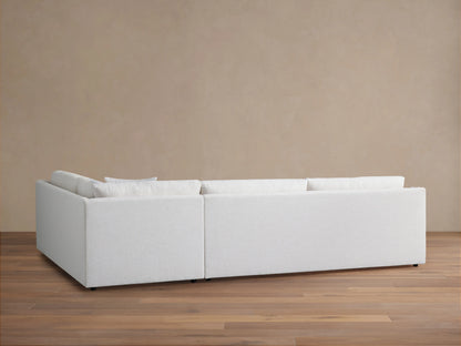 Ashby Two-Piece Sectional in pale fabric, seen from the back against a neutral wall. The sectional's linear design is visible on a wooden floor.