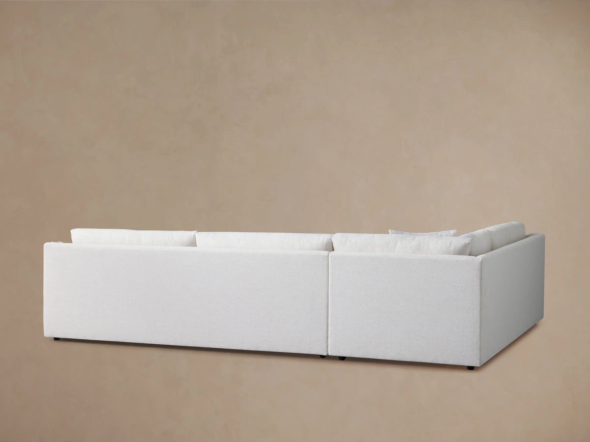 Ashby Two-Piece Sectional in a light beige fabric, featuring a curved armrest, plush backrest cushions, and a smooth seat cushion surface.