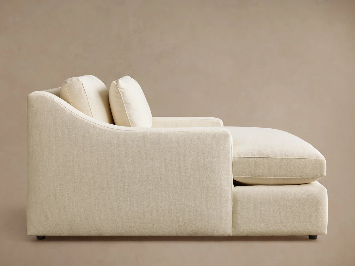 Side profile of the cream Ashby Chaise, featuring a curved backrest, two back pillows, and textured upholstery.