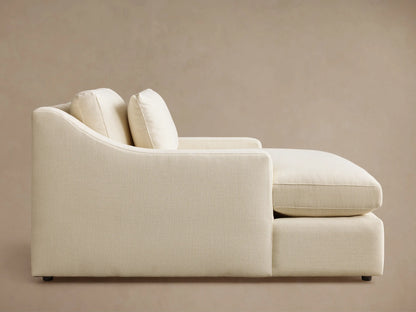Side profile of the cream Ashby Chaise, featuring a curved backrest, two back pillows, and textured upholstery.