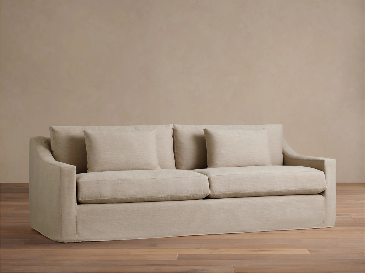 Ashby Slipcovered Sofa in light beige fabric, featuring two seat cushions, two back cushions, and two square throw pillows.