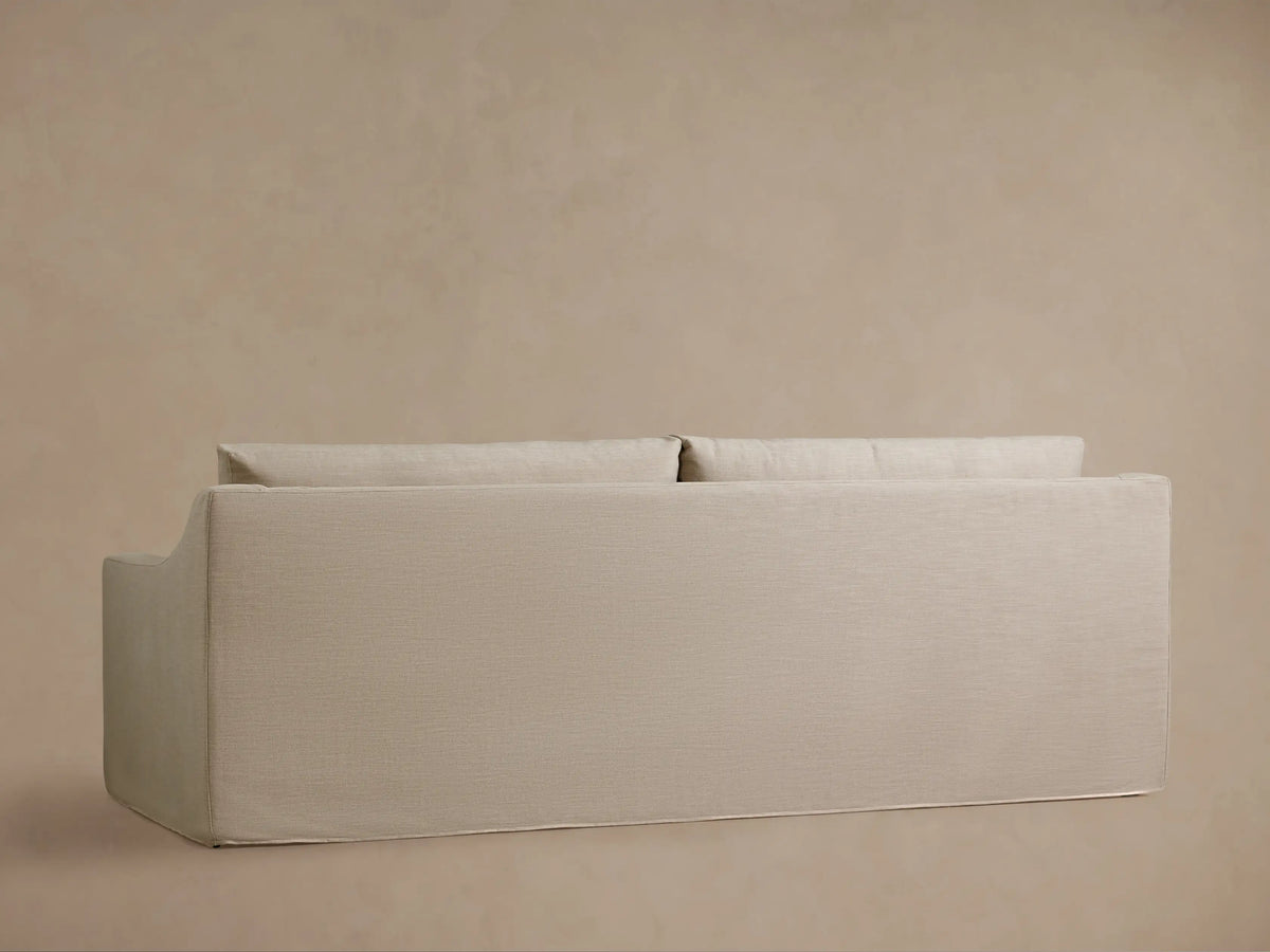 Ashby Slipcovered Sofa in a neutral light beige woven fabric, featuring plush seat and back cushions, with a gently sloped armrest.
