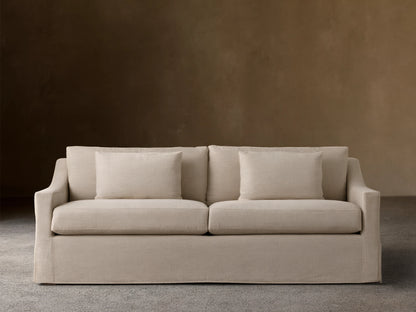 Ashby Slipcovered Sofa in light beige fabric, featuring two seat cushions, two back cushions, and two square throw pillows.