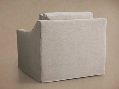 Ashby Slipcovered Swivel Chair with a light beige fabric, shown from the back at an angle. The chair has a boxy shape and visible cushion seams.