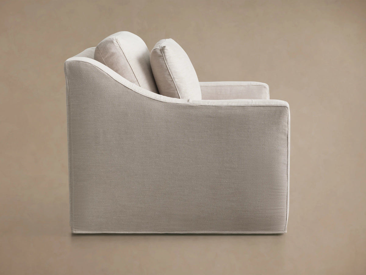 Ashby Slipcovered Swivel Chair in a light beige fabric, shown from the back, highlighting its sleek, rectangular design and subtle stitching.
