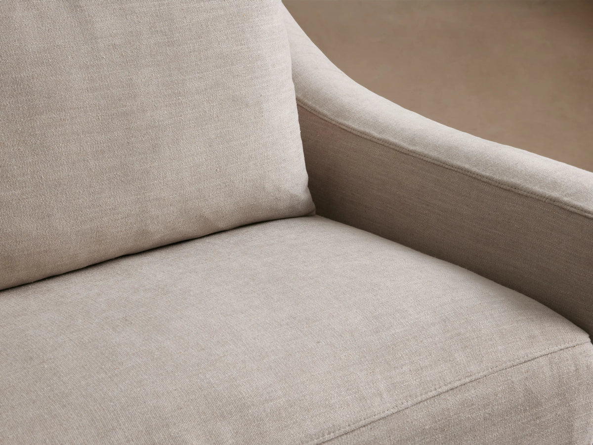 Ashby Slipcovered Swivel Chair in a light beige fabric, featuring a boxy design with padded seat and back cushions on a wooden floor.